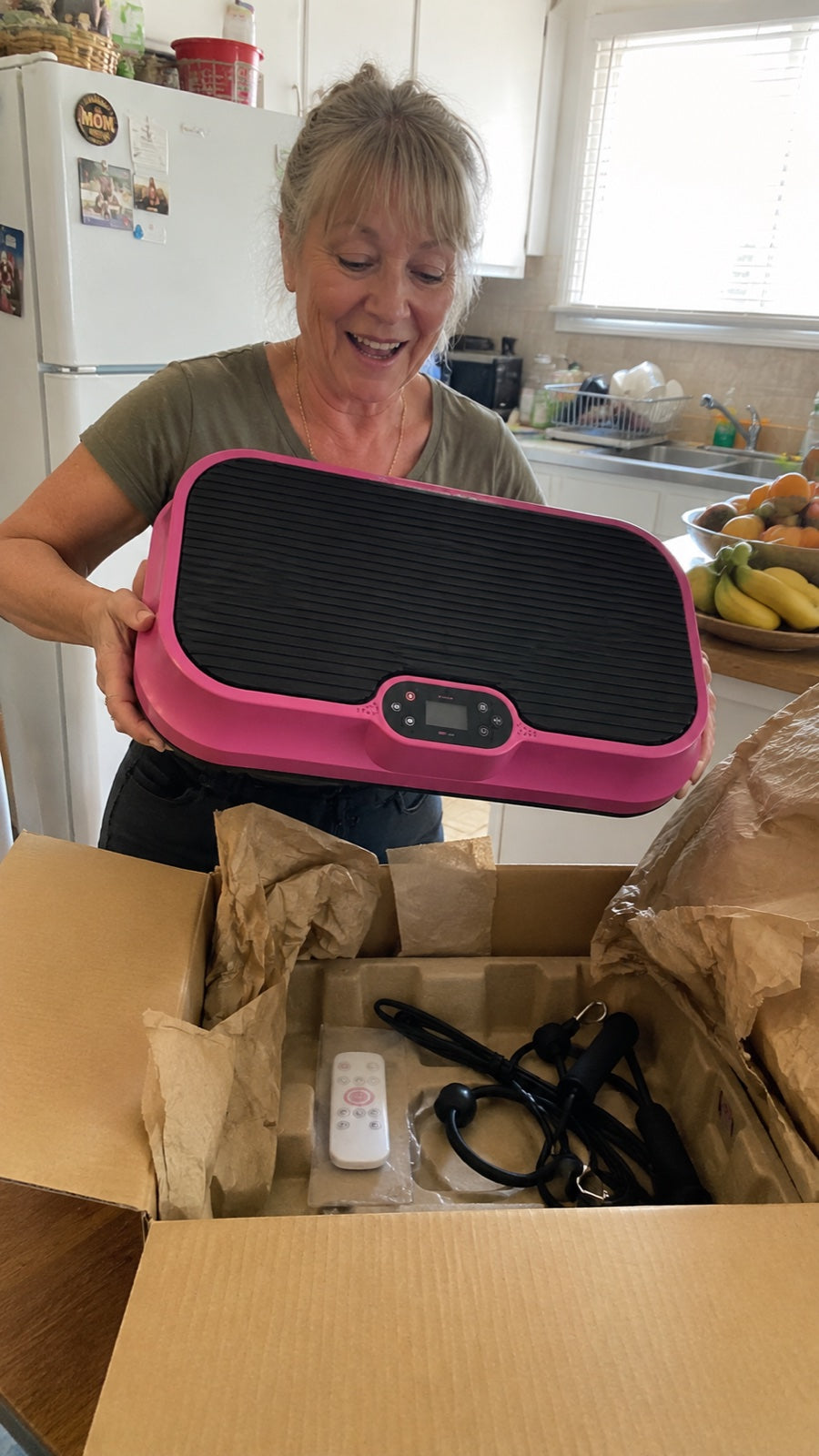Woman lifting the pink Nuvé plate out of its box in her kitchen, remote and bands still packed